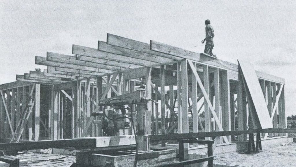 Black and white photo of a wood-frame house with roof trusses going up on a construction site